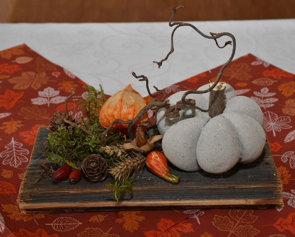 Tischdeko mit Kürbis und Herbstblättern auf Holzbrett